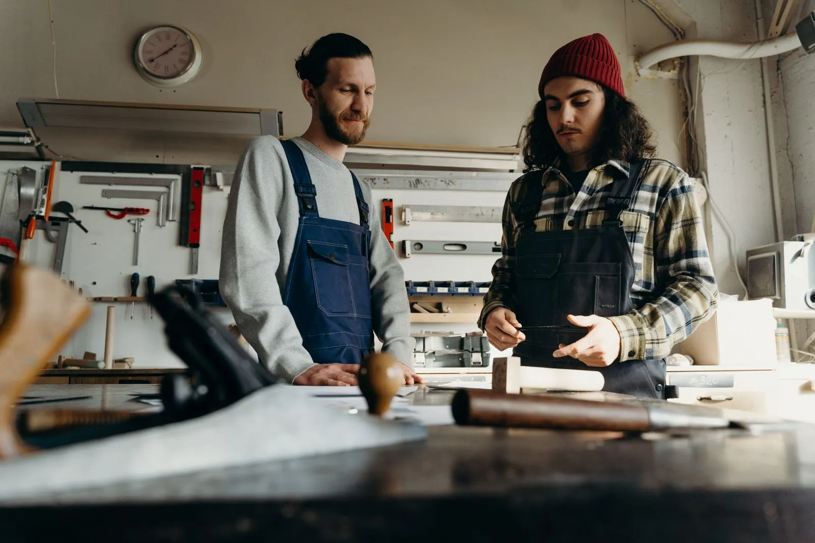 Two carpenters talk through a job at a workshop bench.