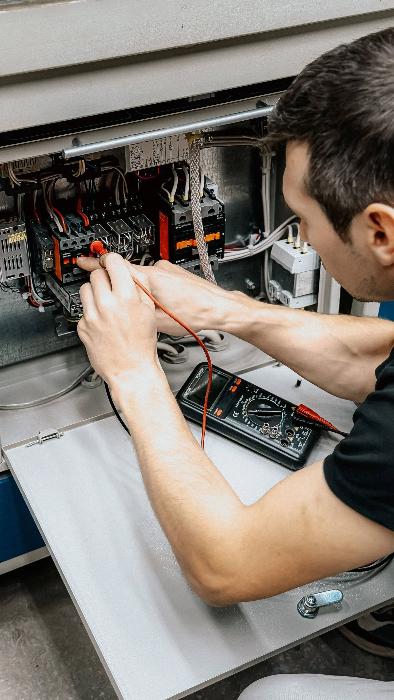 An electrician tests connections in an open switchboard with a multimeter.