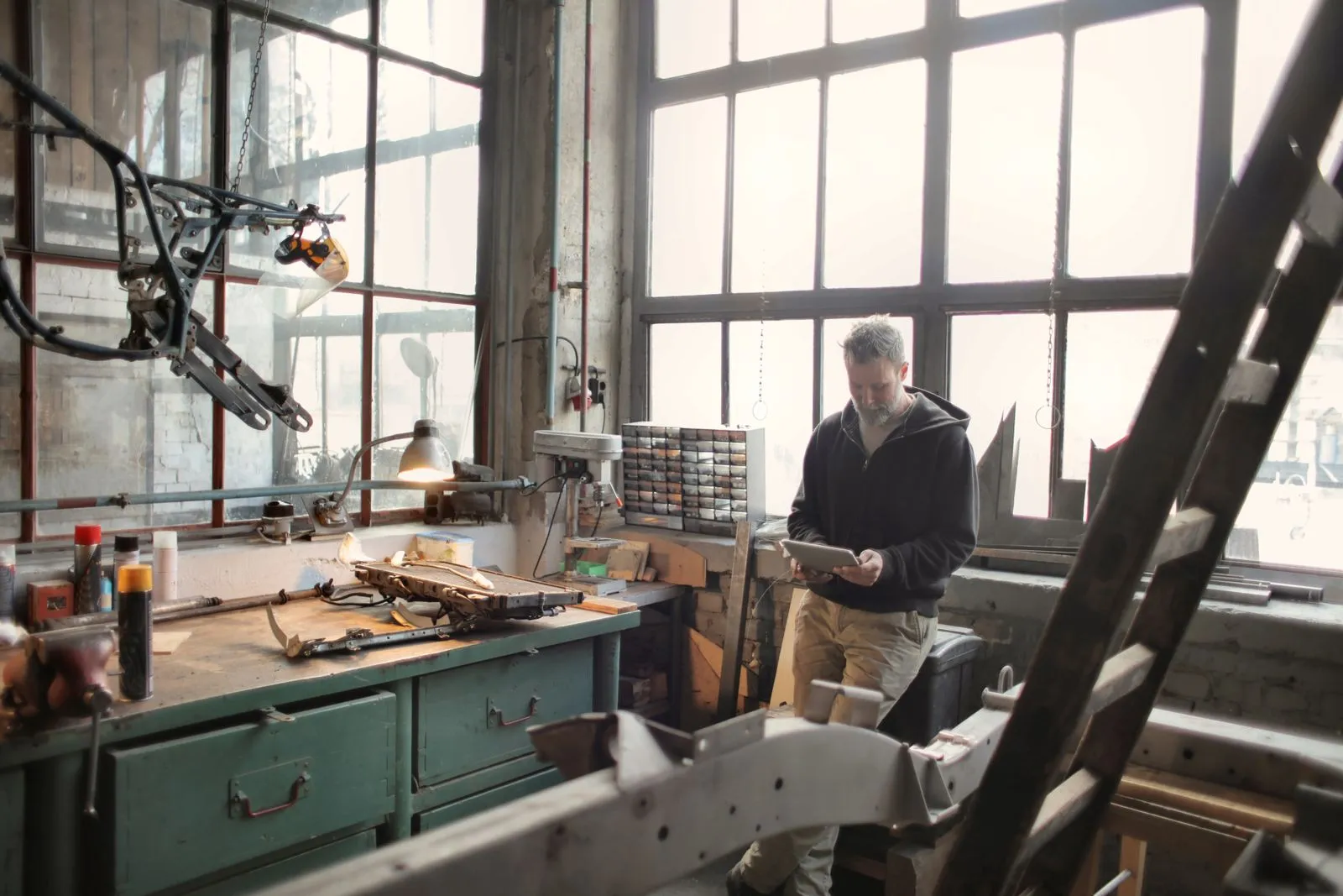 A workshop owner checks a tablet beside a workbench in natural light.
